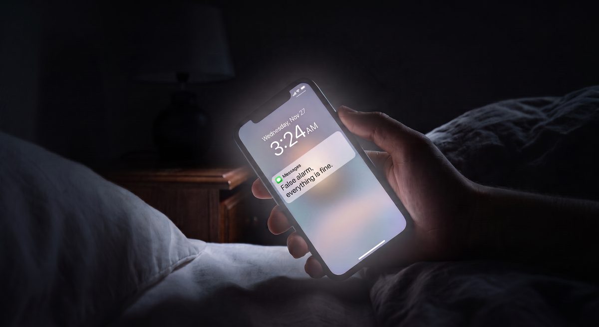 A hand holding a phone in a dark bedroom, the screen showing 3:24 AM